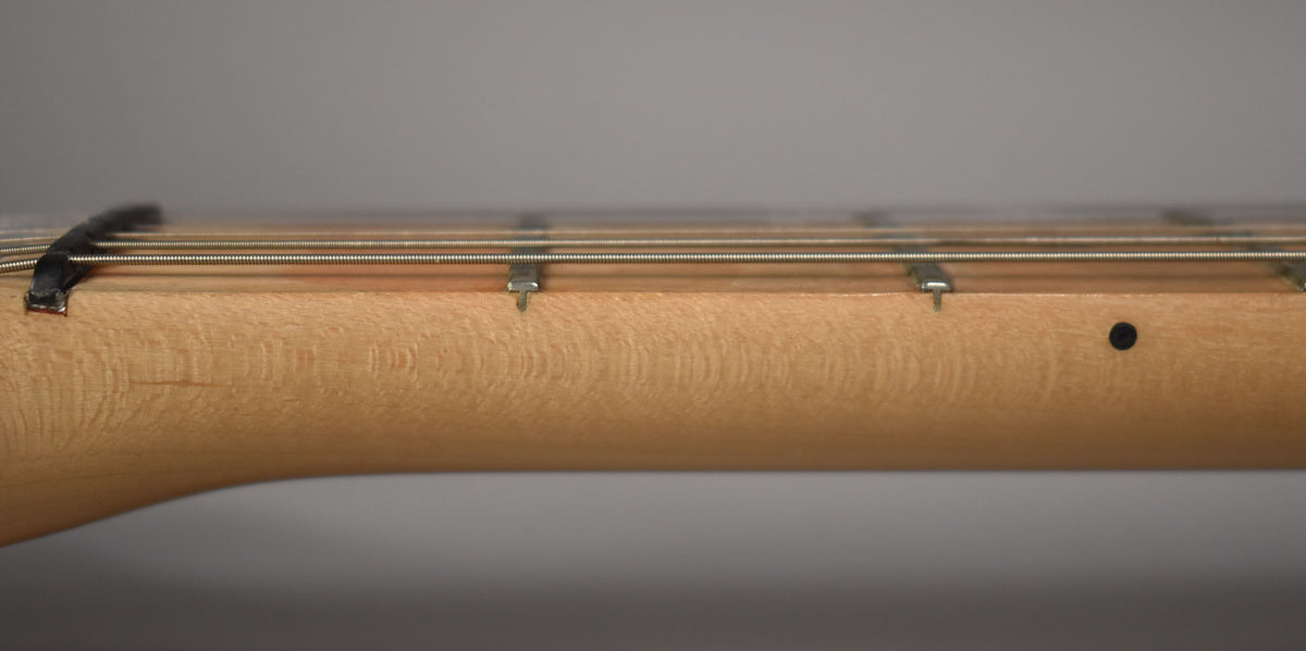 Close-up of the light brown maple neck and fretboard, showing four frets, strings, and a black dot inlay.