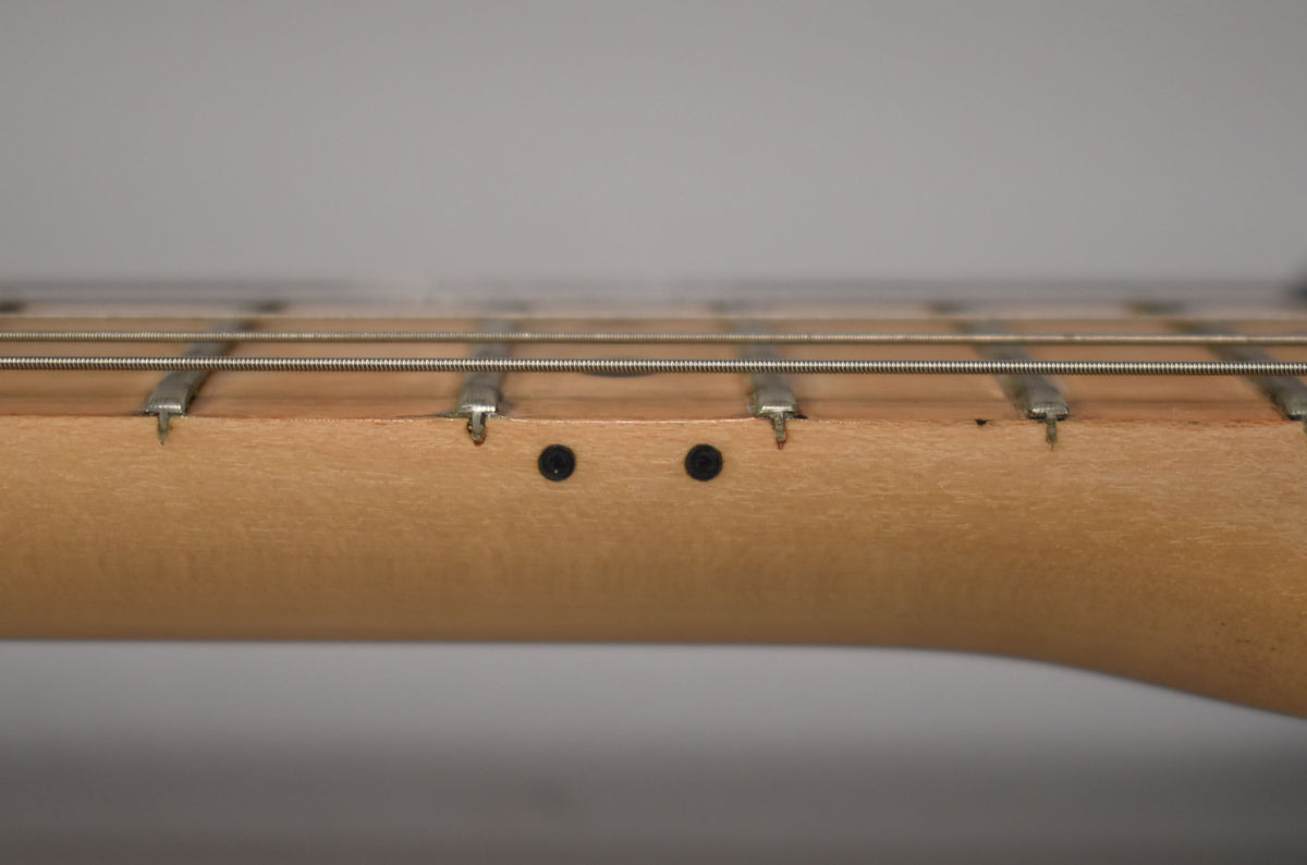 Close-up of the light brown maple neck and fretboard, showing the frets, strings, and two black string trees.