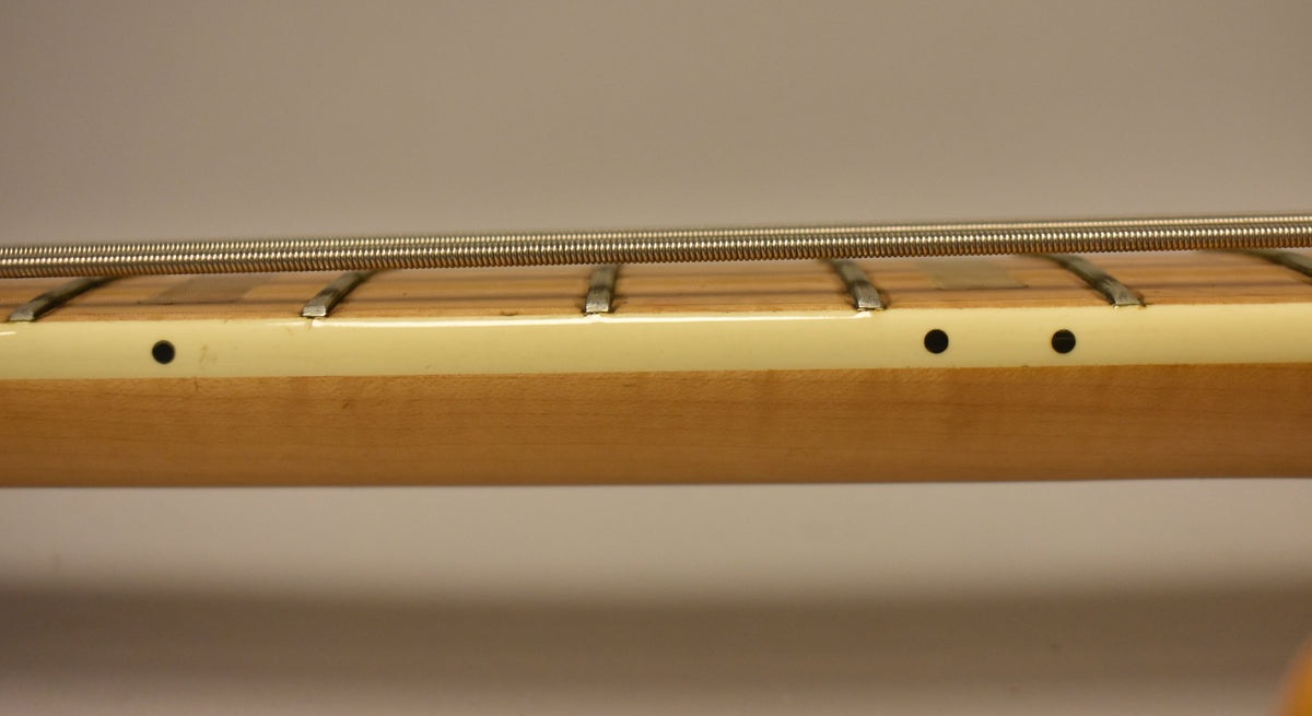 Close-up of the bass neck's maple fretboard and light cream binding, showing four frets, four strings, and three black side dots.