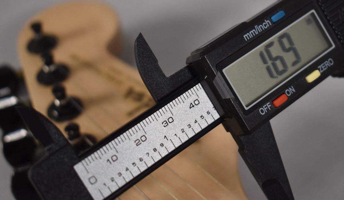 A digital caliper measures the nut width of the natural wood headstock, displaying 1.69 inches.