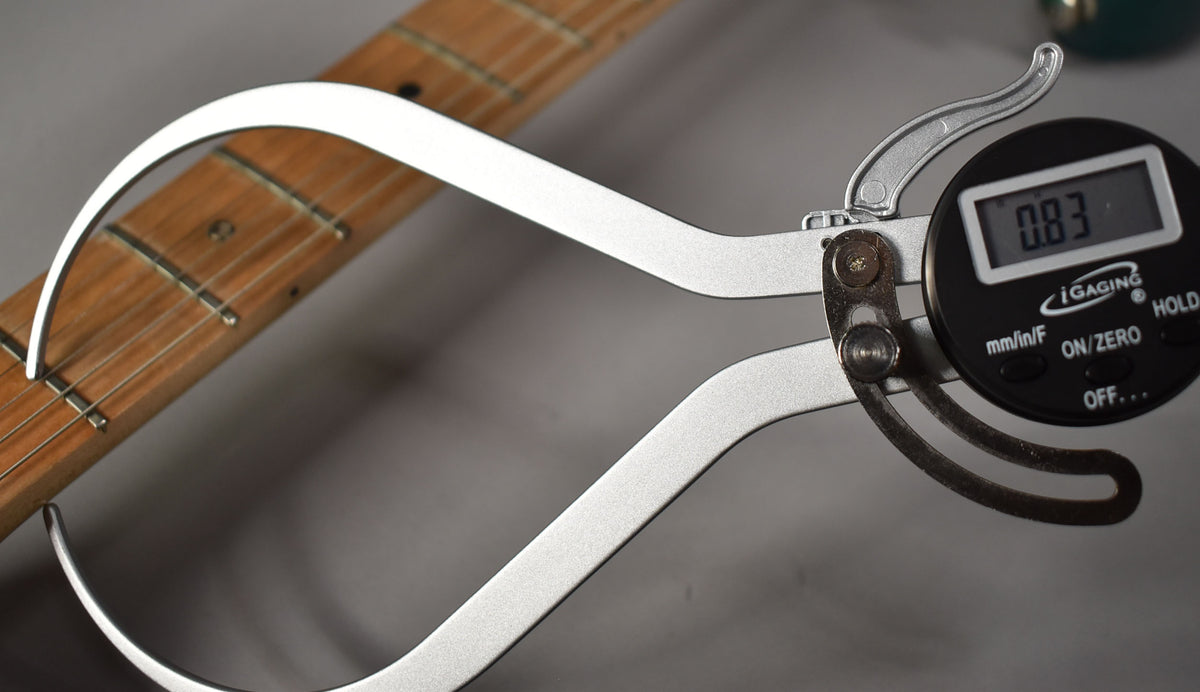 Digital calipers measure the neck thickness at the first fret, showing 0.83 inches, with the fretboard and strings visible.
