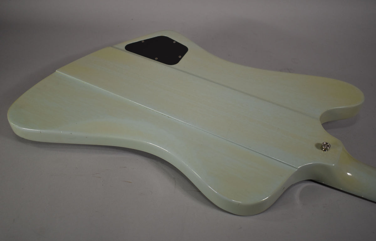 The back of a light blue electric guitar, showing a black control cavity cover and a strap button, with light finish wear.