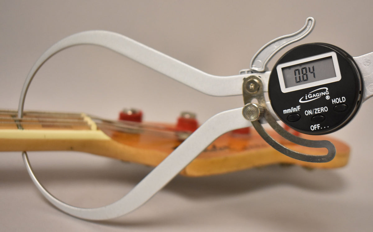 A digital caliper measures the string height at the first fret of the bass, displaying "0.84" mm.