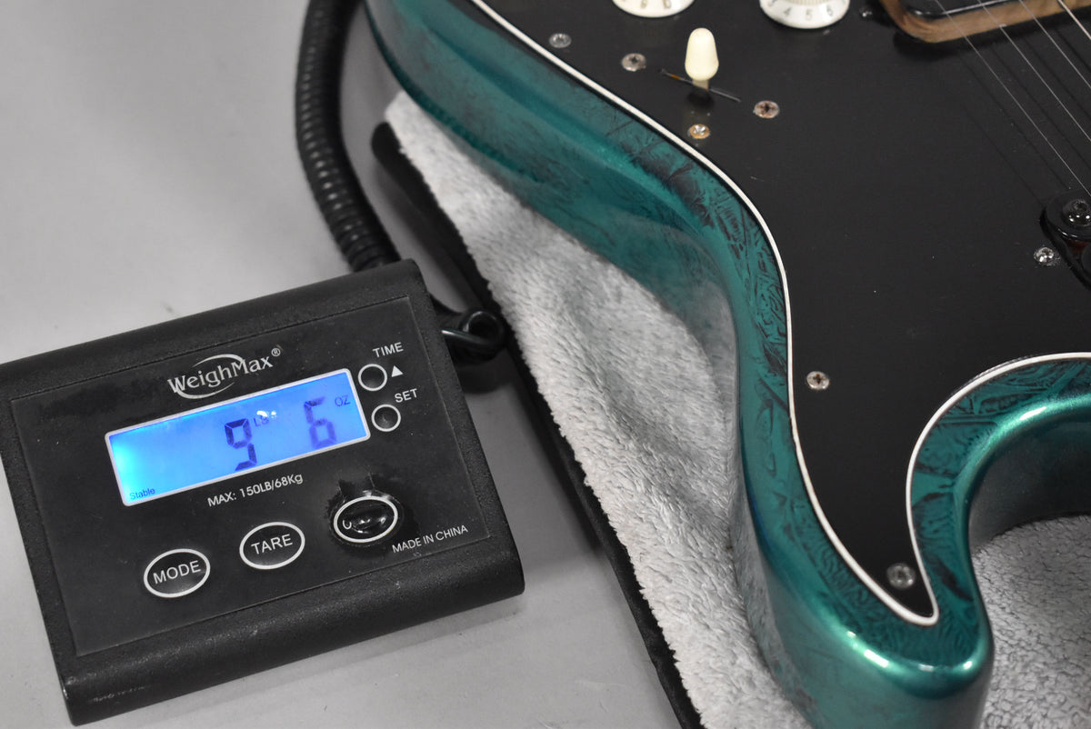 Close-up of the guitar's lower bout on a scale, showing its green flame finish, black pickguard, and white control knobs, reading 9 lb 6 oz.