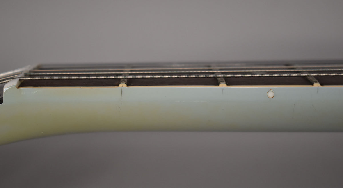 Close-up of the guitar's light blue neck and fretboard, showing finish checking near the frets and a small circular mark.