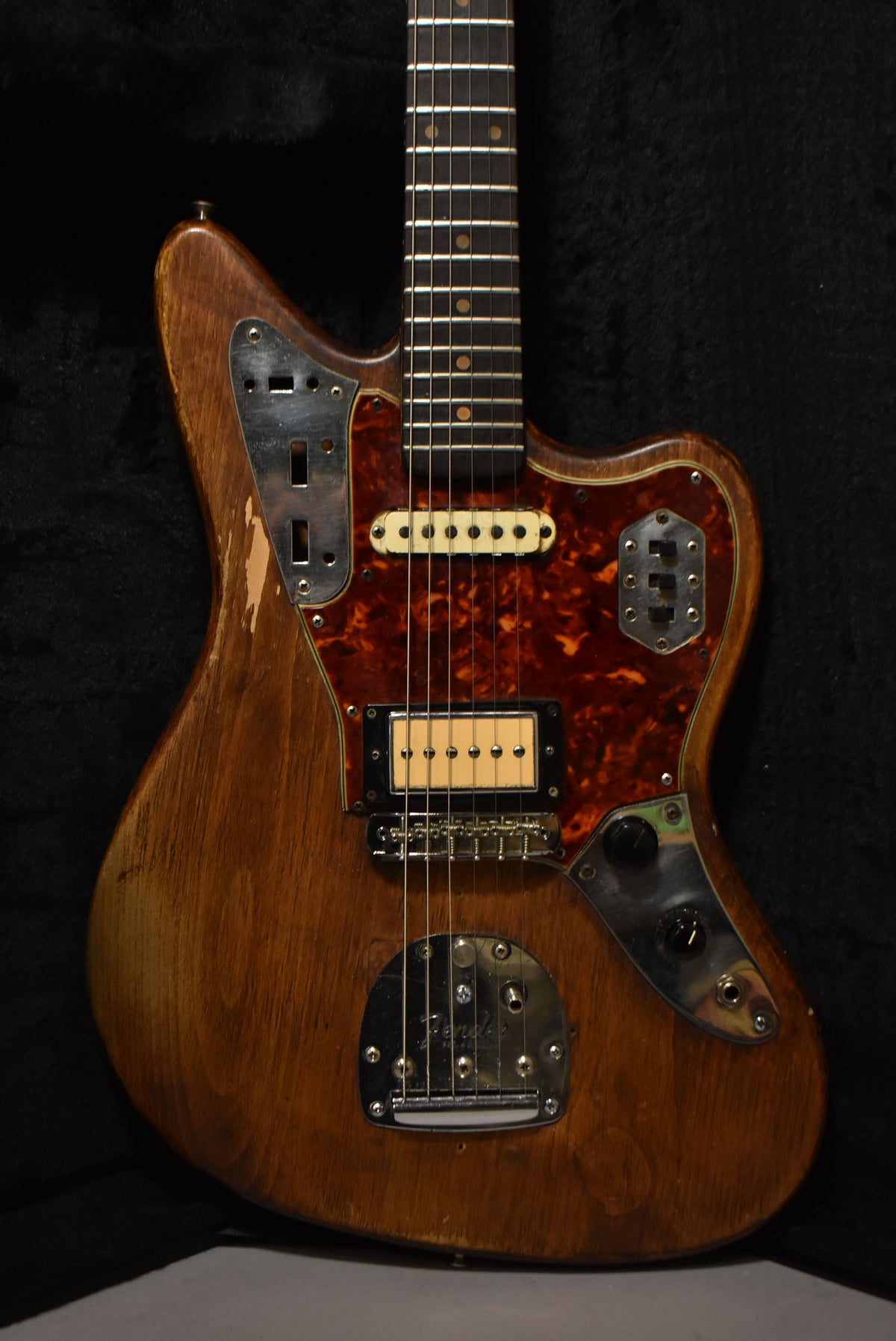 Full-frame view of a natural wood Jaguar with a tortoiseshell pickguard, two pickups, and significant wear on the upper horn.