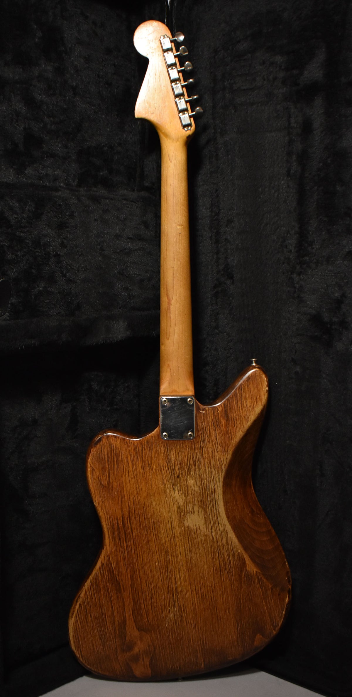 Rear view of a natural wood guitar with a light brown neck, chrome tuners, and a worn, textured body.