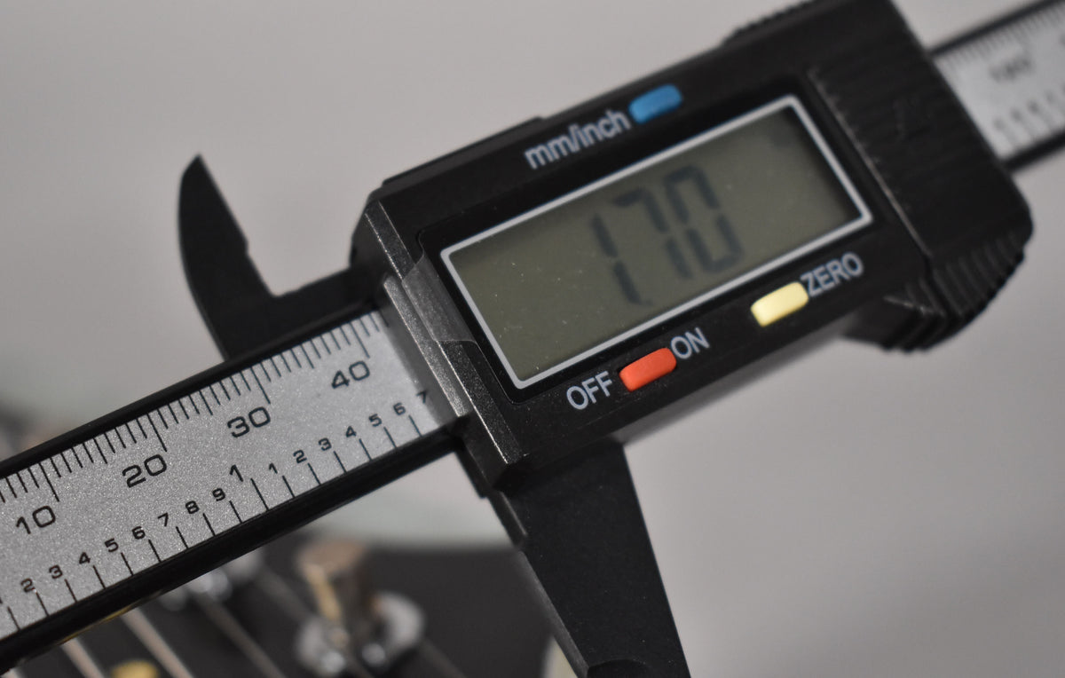 A digital caliper measures the guitar's nut width, displaying "1.70" on its screen, with the fretboard visible below.