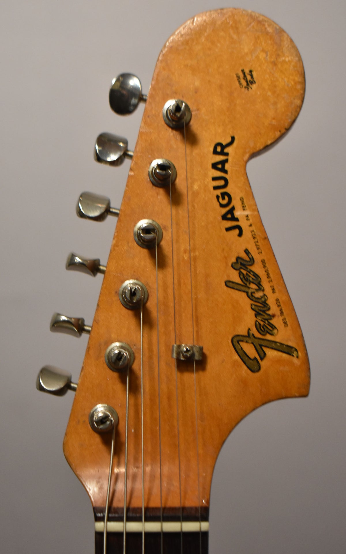 Close-up of the guitar's natural-finish headstock, showing six chrome tuners, a string tree, and visible wear and checking.