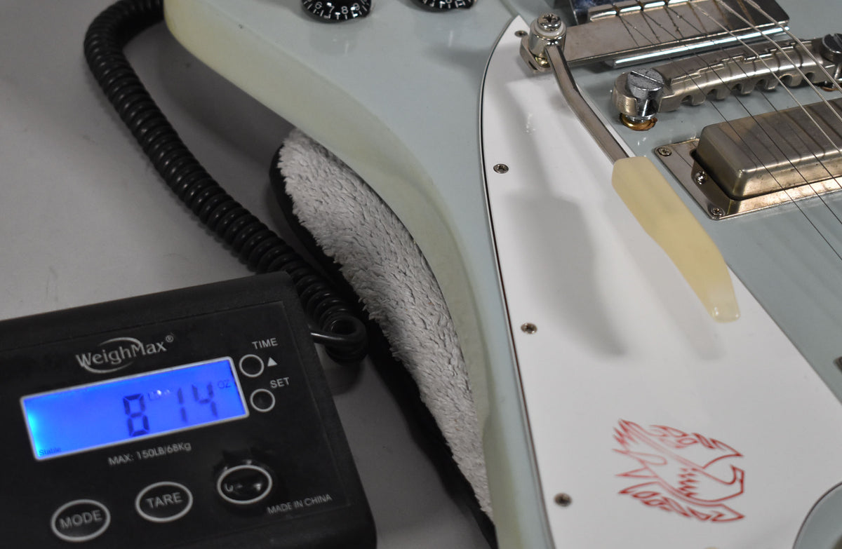Close-up of the guitar's lower body on a scale reading 8 lbs 14 oz, showing the white pickguard with red bird graphic.