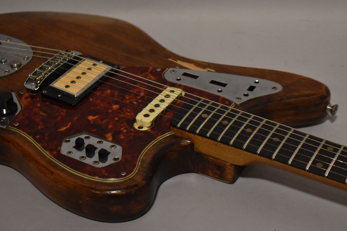 Close-up of a natural wood Jaguar with a tortoise pickguard, a cream humbucker, and a single-coil pickup, showing body wear.