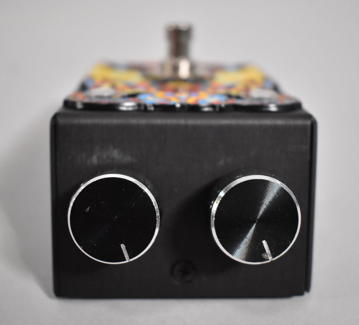 Front view of the black pedal, showing two large, round, silver-rimmed control knobs and light scuffs on the matte finish.