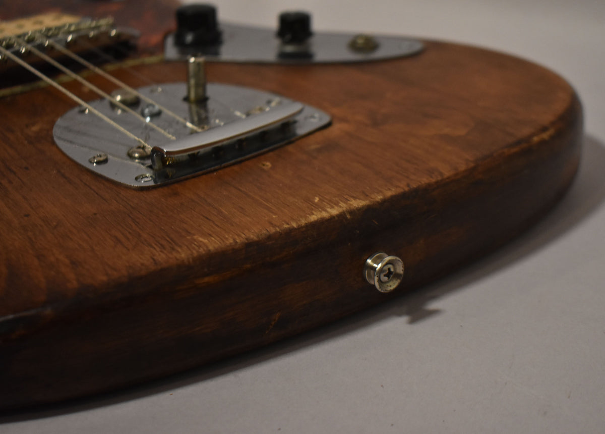 Close-up of the guitar's lower body, showing the natural wood finish, chrome vibrato, and strap button with visible wear and scratches.