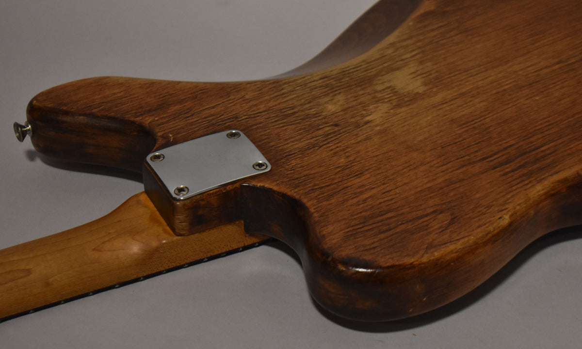 The guitar's natural wood body, with visible grain and wear, meets a light-colored neck at a chrome neck plate.