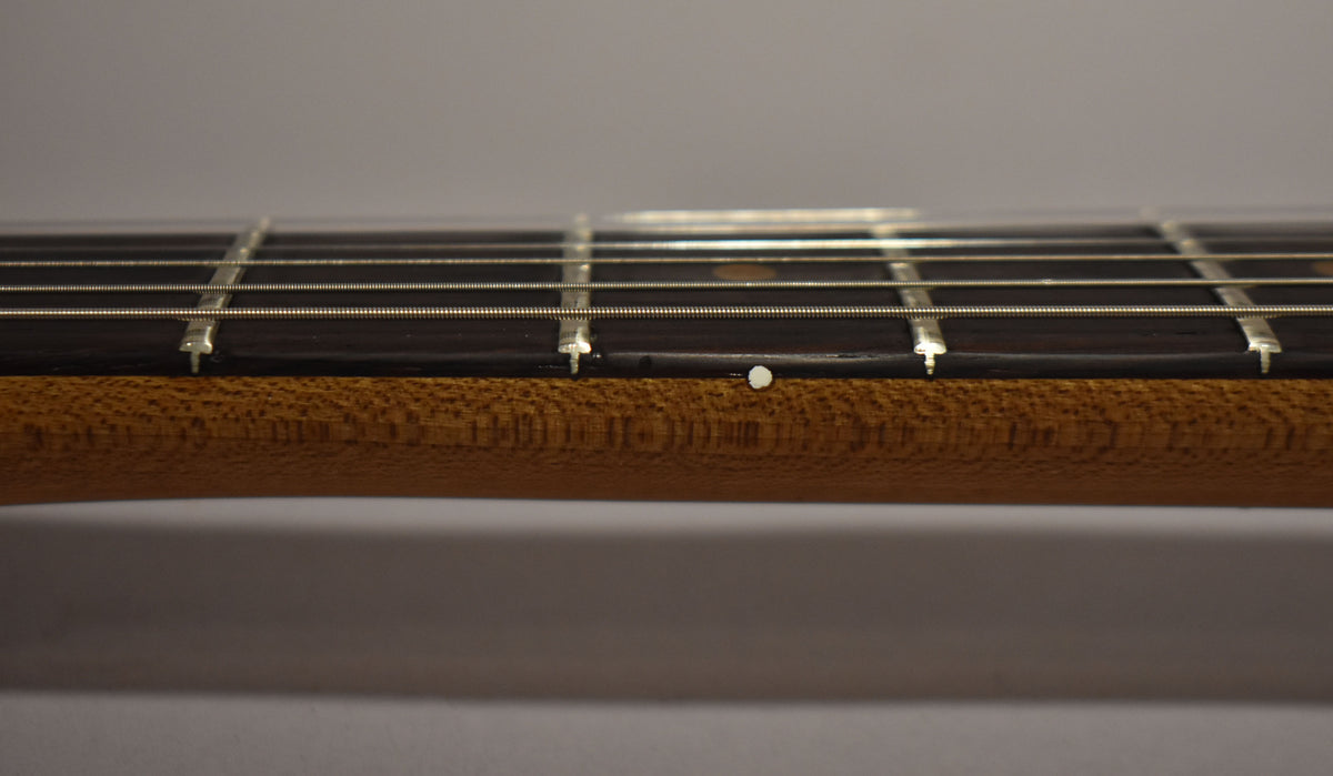 The guitar's dark fretboard and light brown neck are viewed from the side, showing a white dot inlay and fret wear.