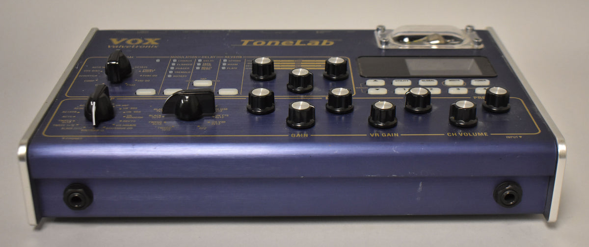 A blue effects pedal, viewed from the front-right, showing its top panel with black knobs, white buttons, a screen, and a clear tube.