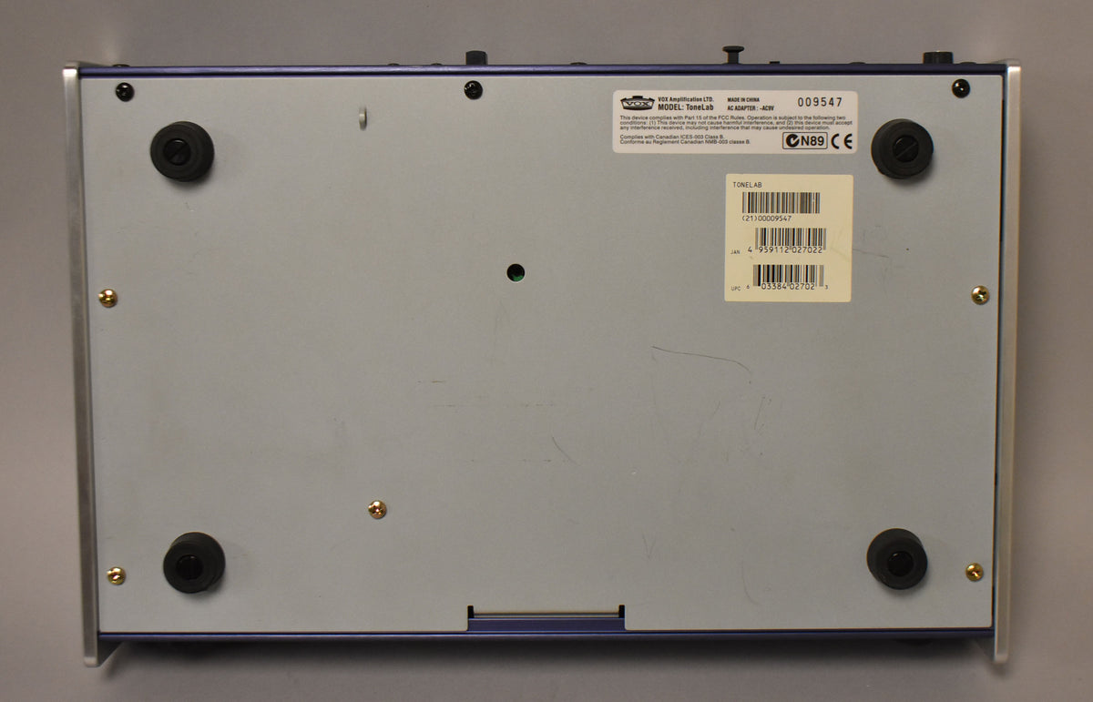 The blue effects pedal is shown from the bottom, revealing a light gray base plate with four black rubber feet and gold screws.