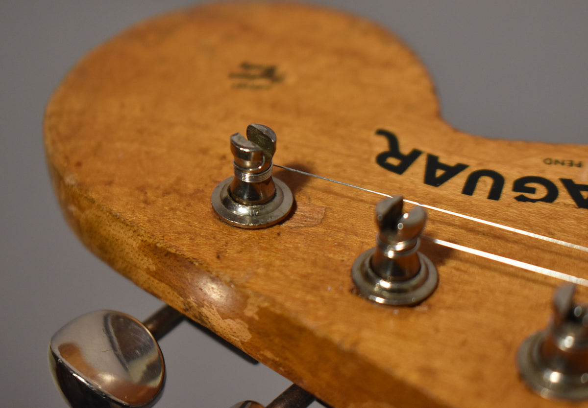 Close-up of the natural wood headstock, showing two chrome string trees, a tuning peg, and heavy finish wear along the bottom edge.