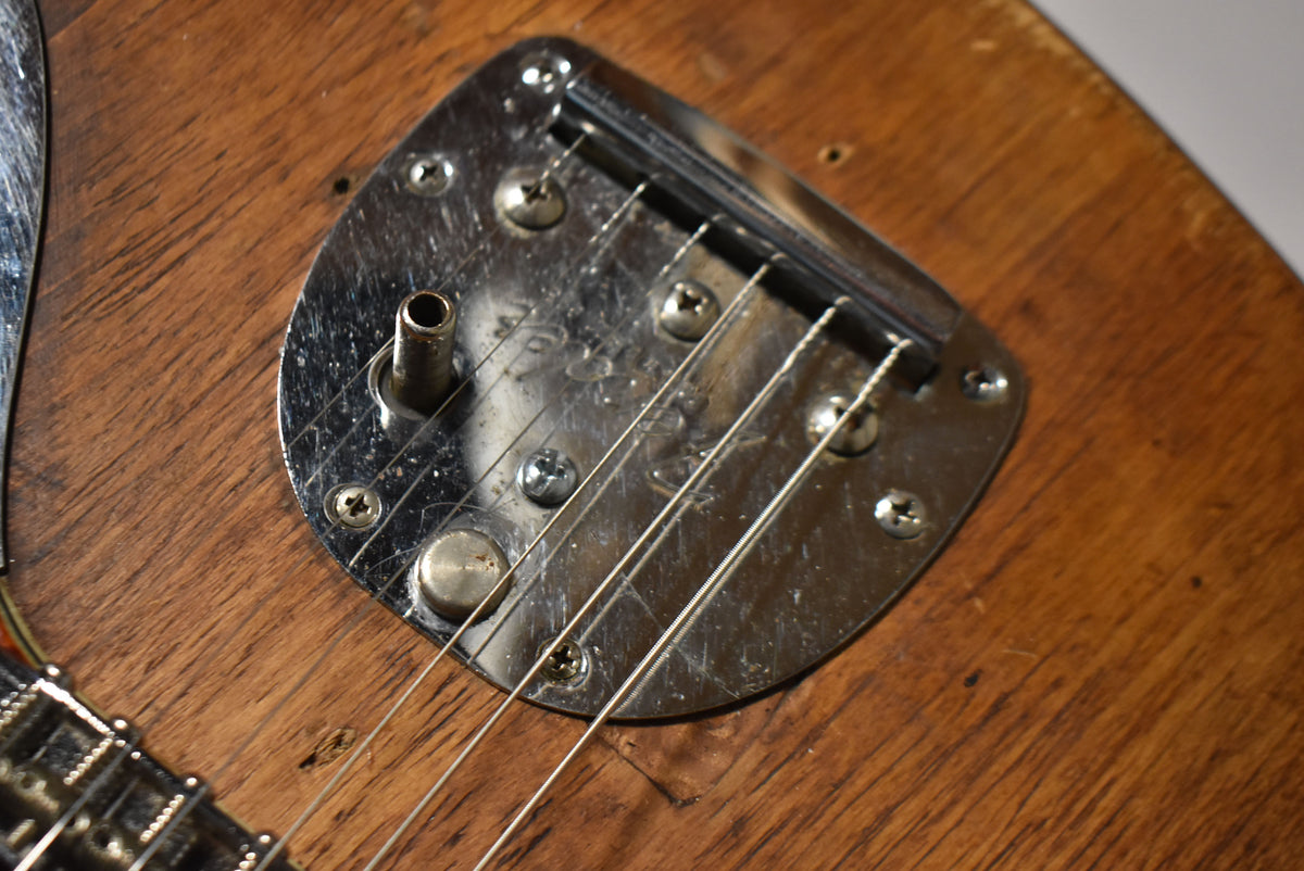 Close-up of the guitar's worn chrome vibrato tailpiece and arm socket, showing heavy scratching on the natural wood body.