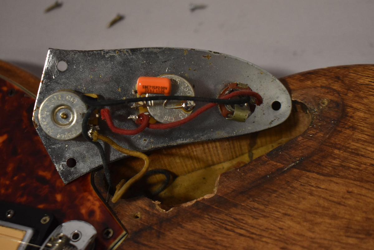 Close-up of the guitar's control cavity, revealing exposed wiring, an orange capacitor, and three potentiometers on a worn metal plate.