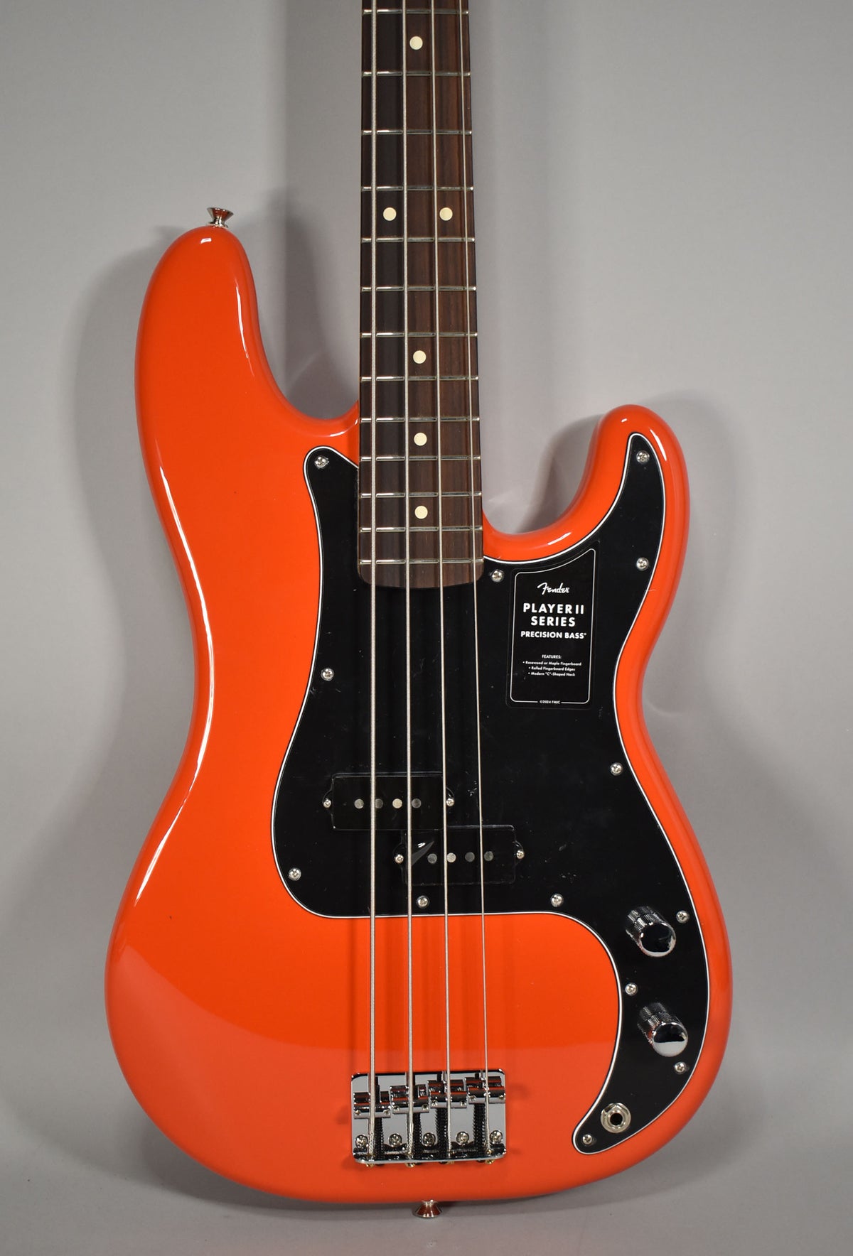 The coral red bass, with a glossy finish, is shown from the upper body to the bridge, featuring a black pickguard and chrome hardware.