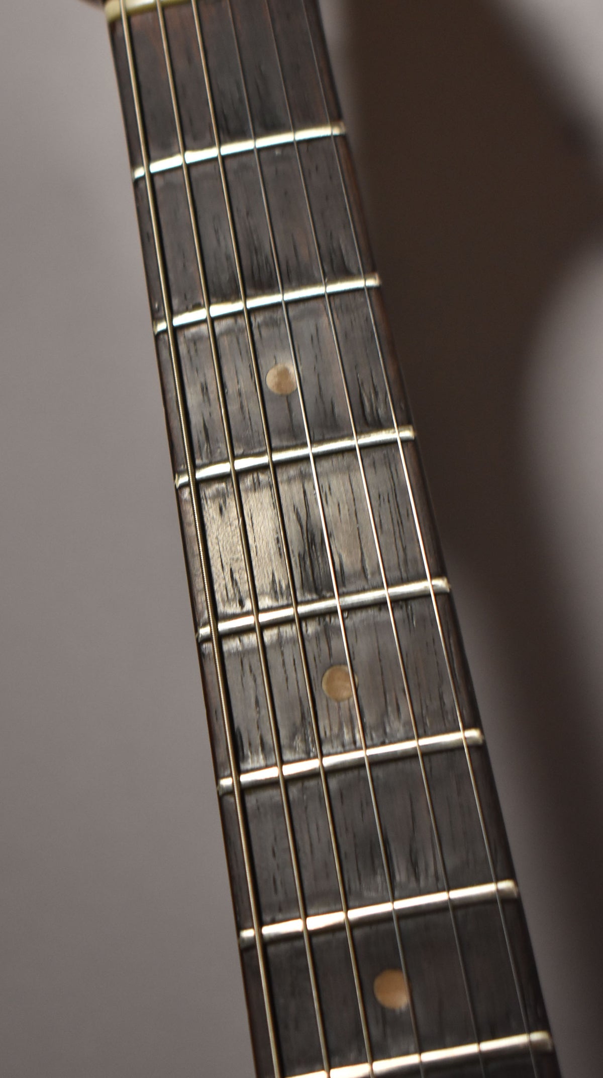 Close-up of the dark rosewood fretboard with light wear, showing frets 1-7 and three light-colored dot inlays.