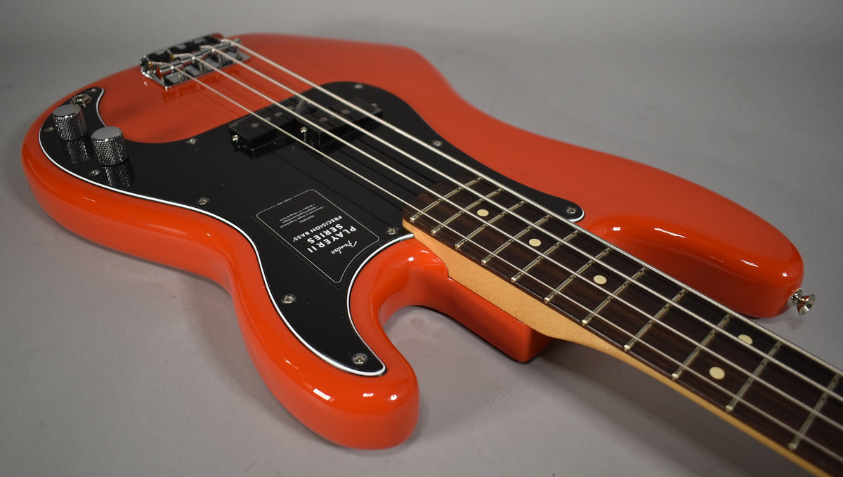 Coral red bass, angled from the upper left, showing the glossy body, black pickguard, chrome bridge, and two knurled control knobs.
