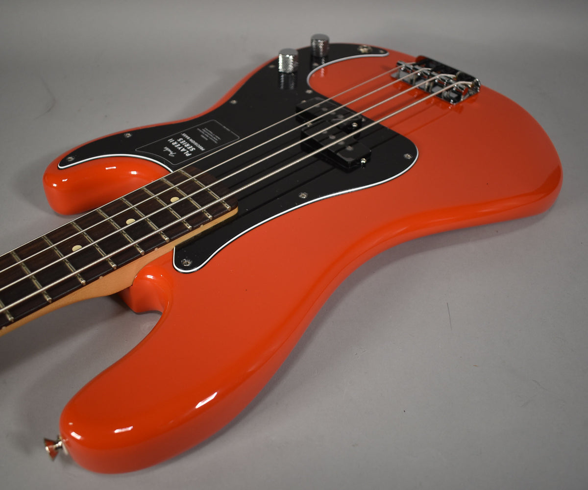 Coral red bass with a glossy finish, black pickguard, chrome hardware, and a rosewood fretboard, viewed from the upper body.