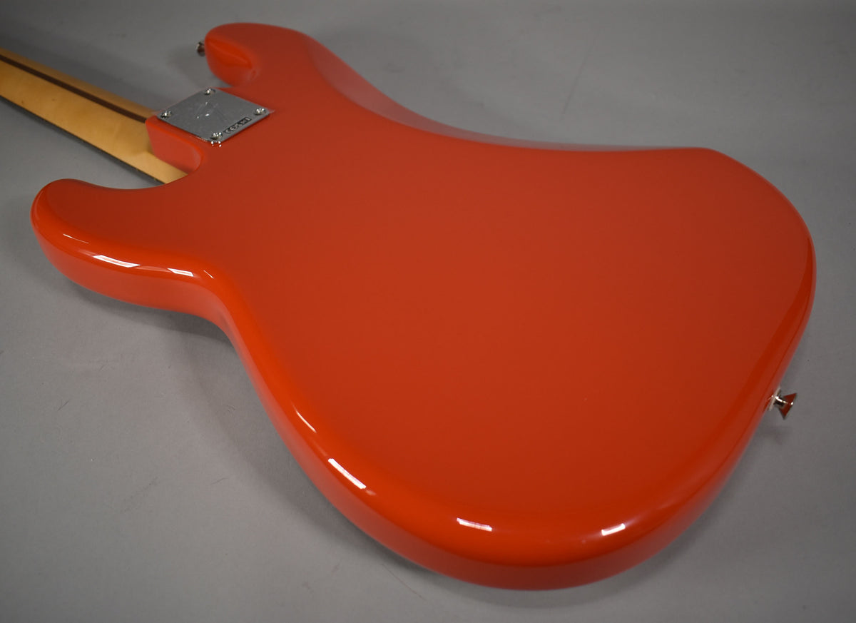 The back of a glossy coral red bass body, angled from the neck joint to the lower bout, with a chrome neck plate and strap button.