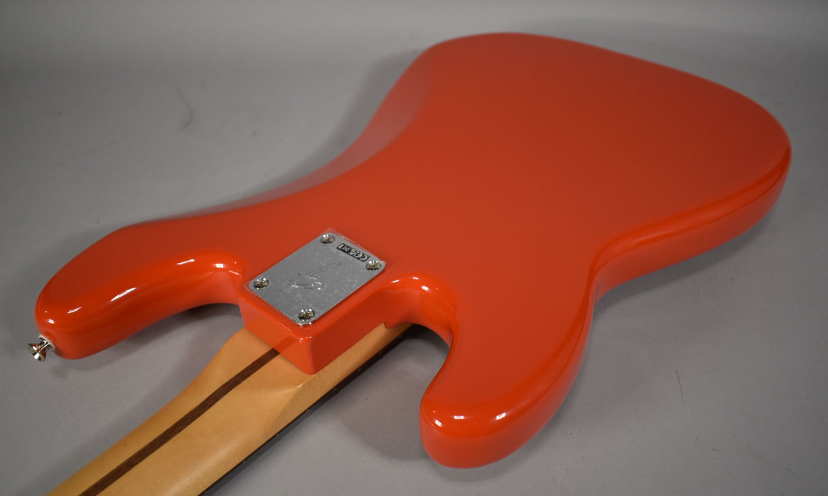 The back of a glossy coral red bass body, angled from the lower left, with a chrome neck plate and a light wood neck.
