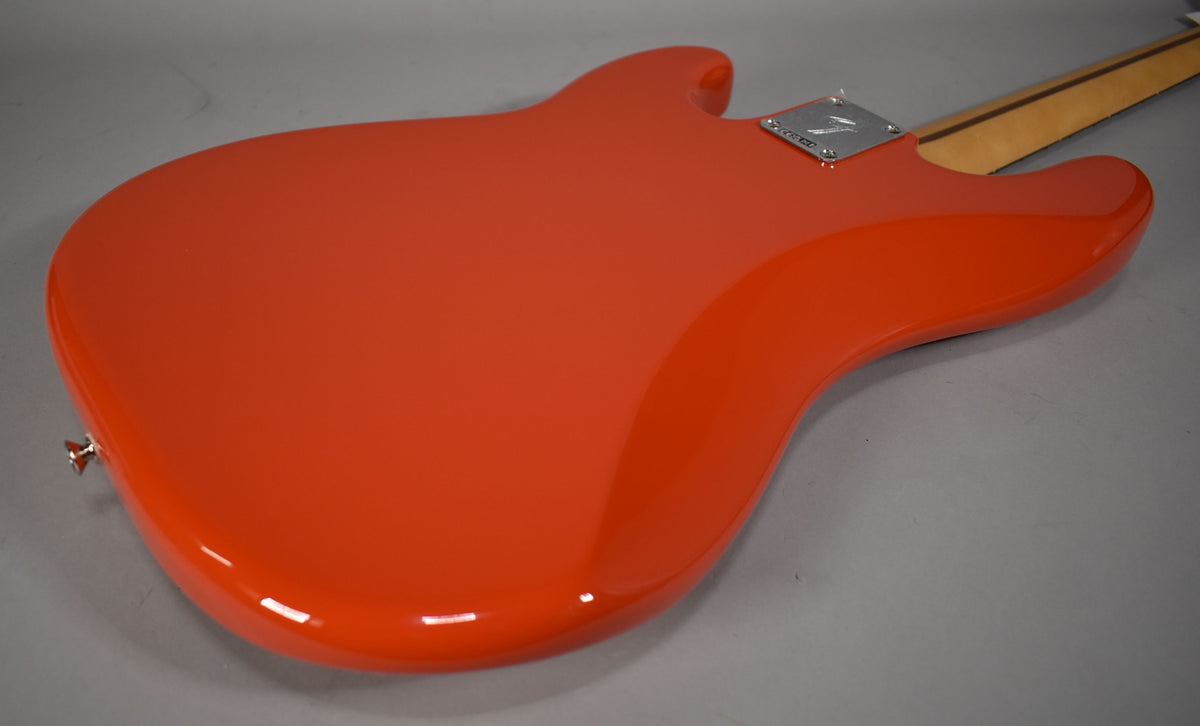 The back of a glossy coral red bass body is shown from an angle, with a chrome neck plate and strap button visible.