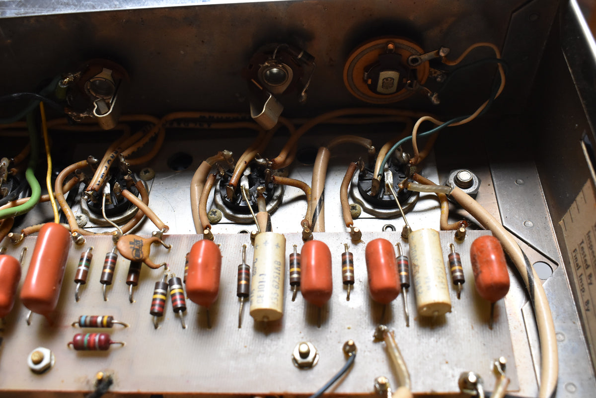 Close-up of the amp's internal wiring, showing a circuit board with orange and cream capacitors, resistors, and tube sockets.
