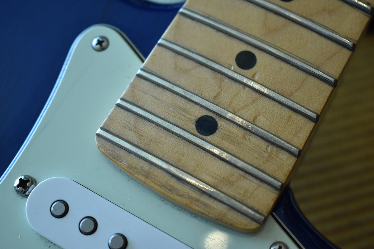 Close-up of the maple fretboard with black dot inlays, showing light wear and grime on the frets and wood, over a mint green pickguard.