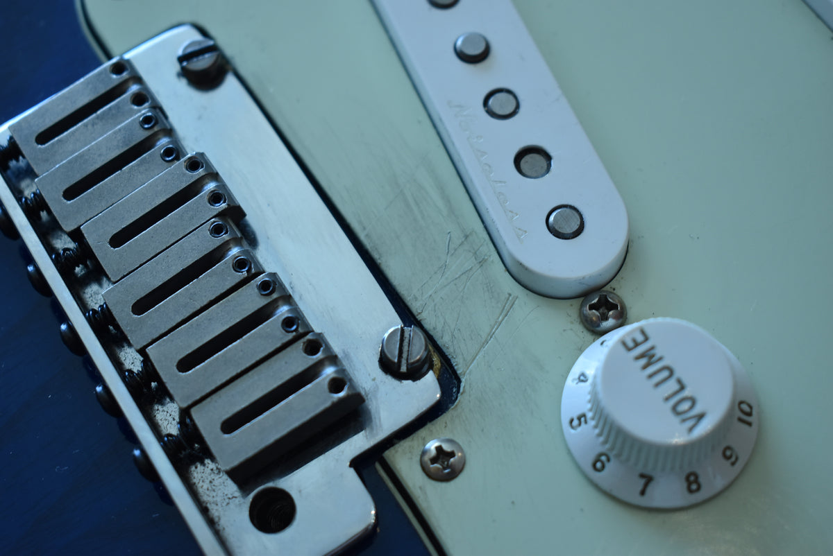 Close-up of the sapphire blue body, showing the chrome bridge, white pickguard with a single coil pickup, and a white volume knob.