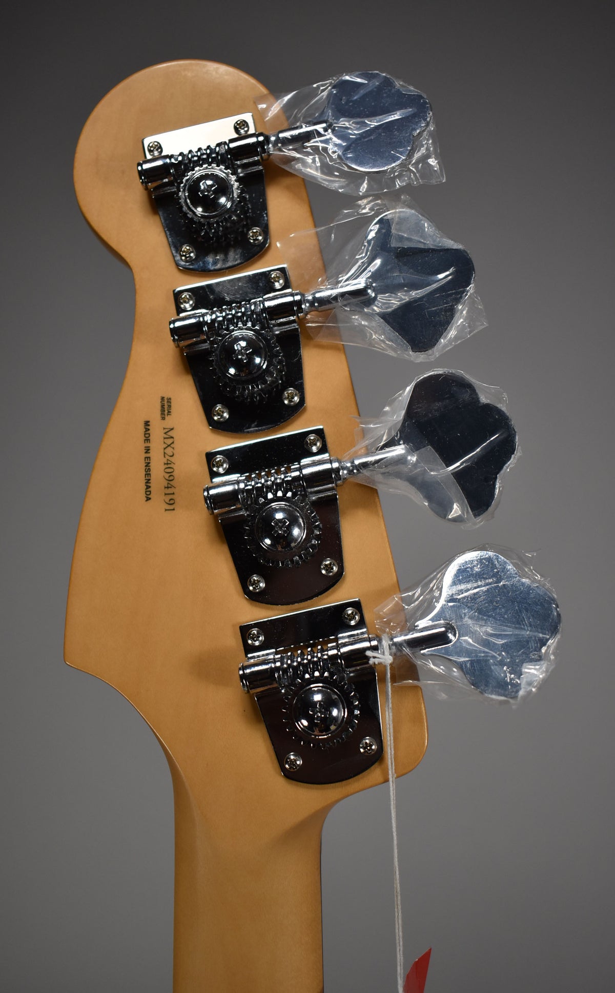 Rear view of the bass headstock, showing four chrome tuners with their paddles still in plastic wrapping.