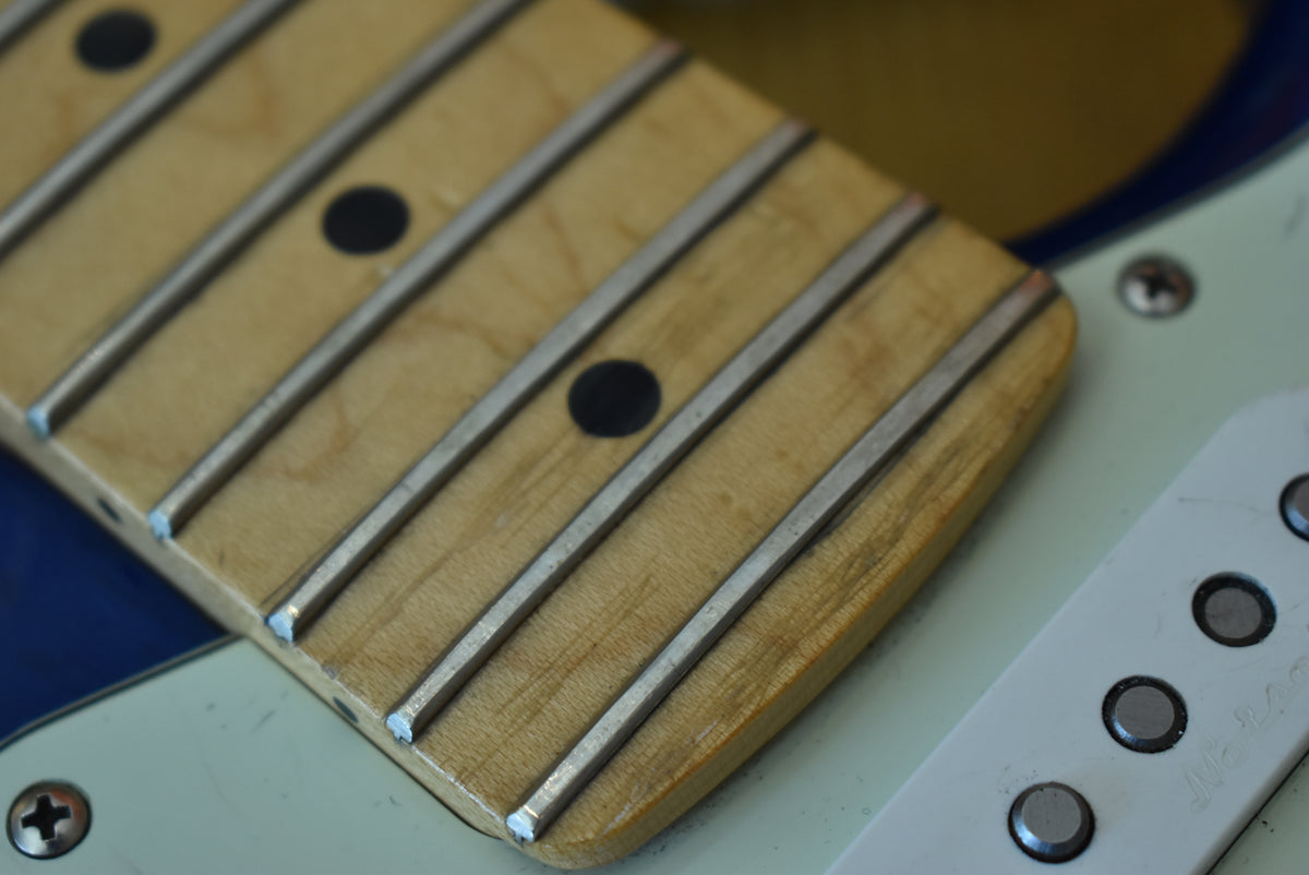 Close-up of the maple fretboard with dark dot inlays and frets, next to a white pickup with visible pole pieces.