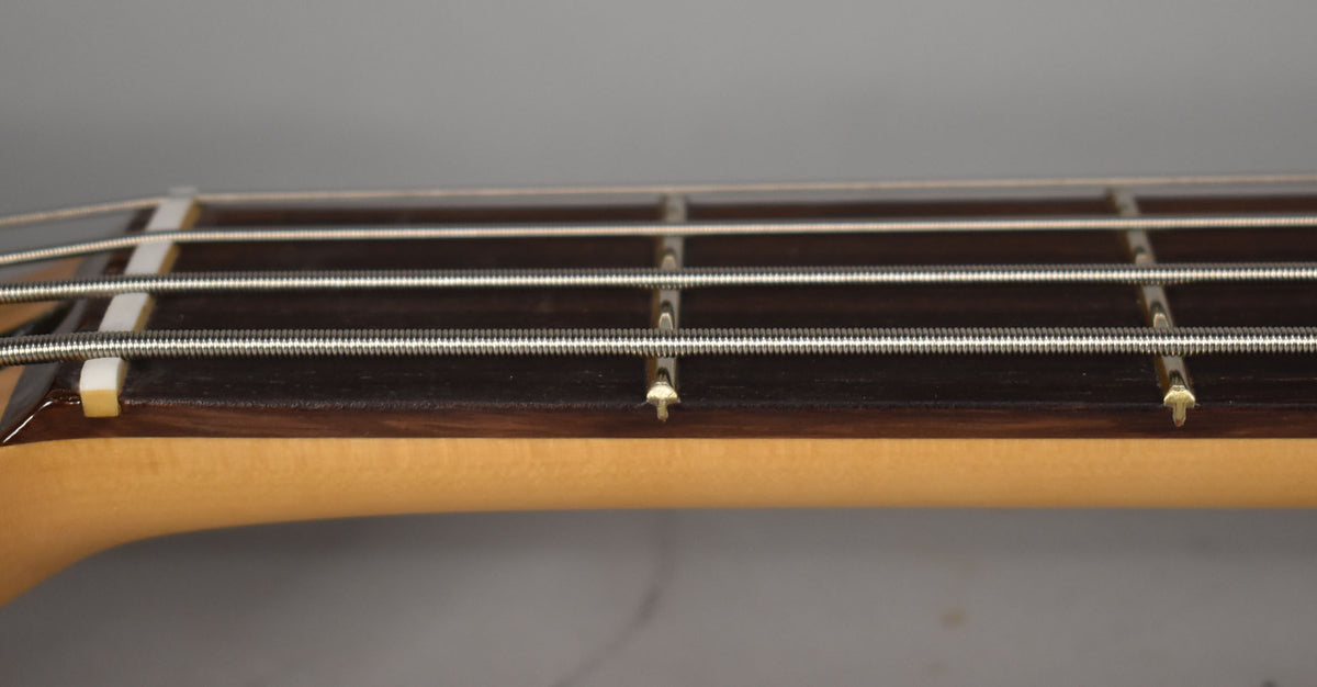 Close-up of the bass's dark fretboard and light maple neck, showing the first four frets, strings, and white nut from the side.