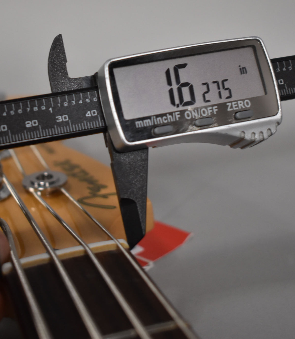 A digital caliper measures the bass nut width at 1.6275 inches, with the headstock and strings visible below.