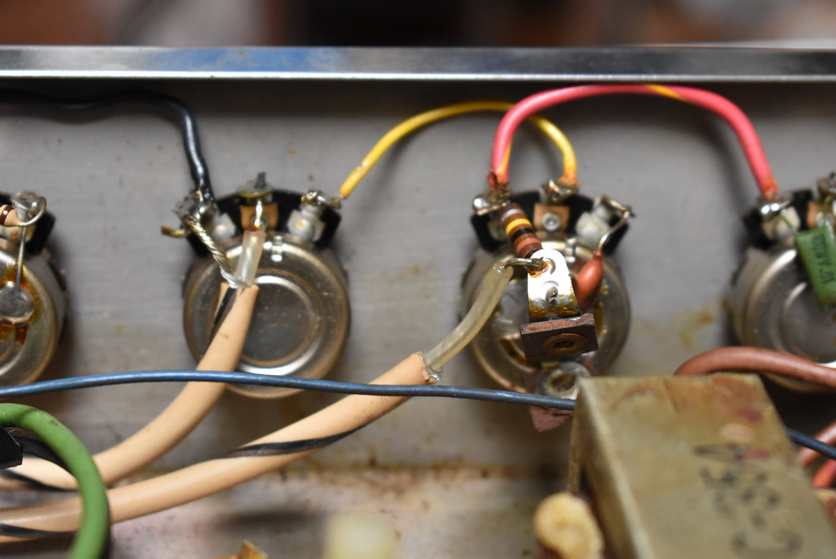 Close-up of the amp's internal wiring, showing four silver potentiometers with colorful wires, resistors, and capacitors, all with visible rust.