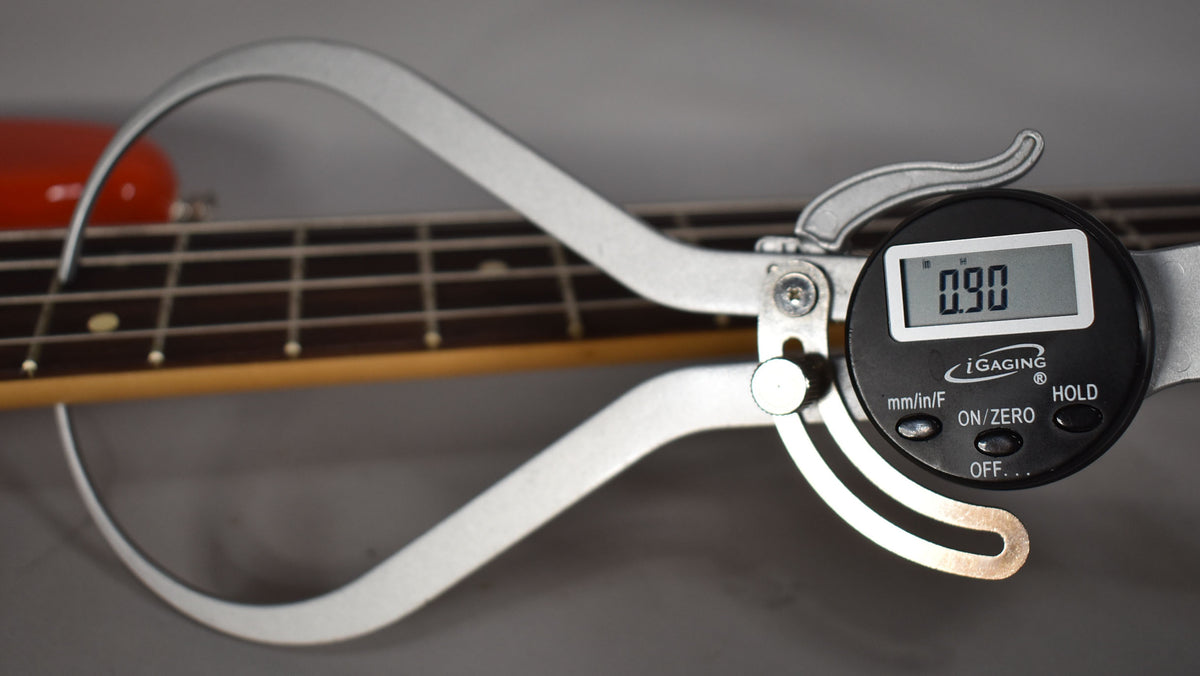 A digital caliper measures the bass's fret height at 0.90mm, with the coral red body visible in the background.