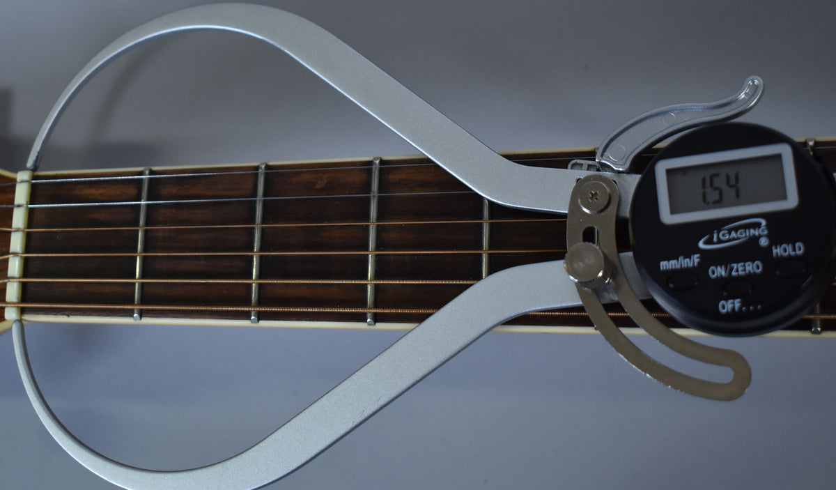 A digital caliper measures the guitar's dark brown fretboard, showing a reading of 1.54, with bronze strings and metal frets.