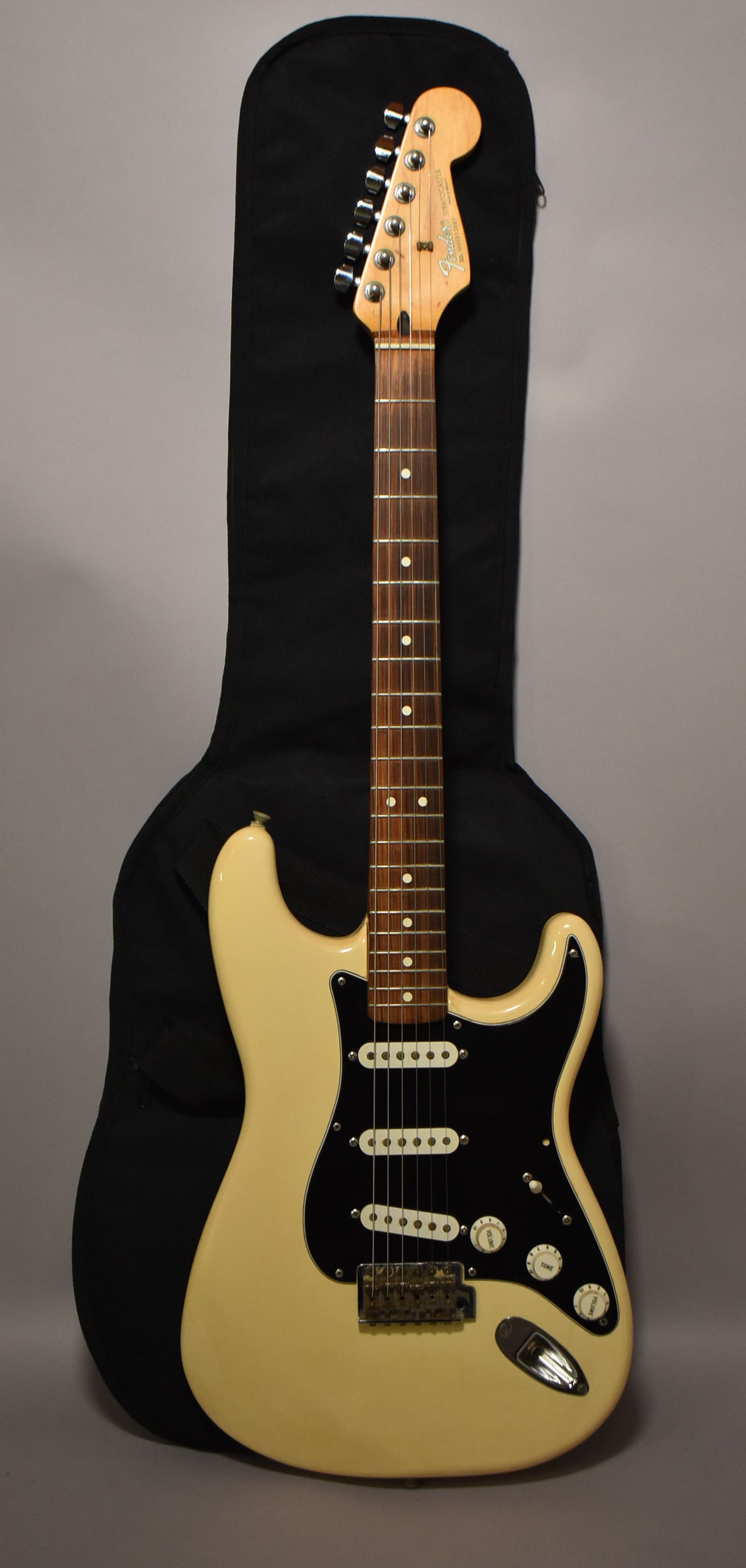Full-length view of a cream-colored electric guitar with a black pickguard, three single-coil pickups, and a rosewood fretboard.