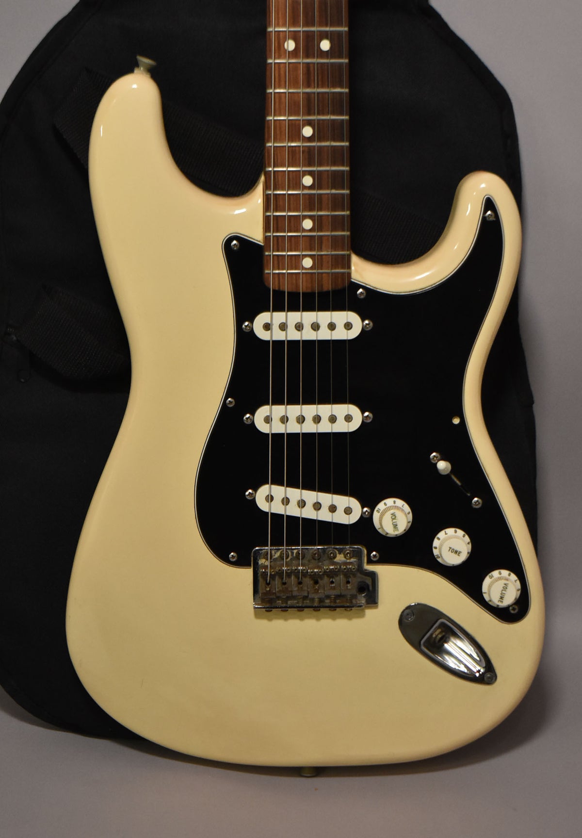 Full-frame view of an off-white Stratocaster with a black pickguard, three white single-coil pickups, and a chrome tremolo bridge.