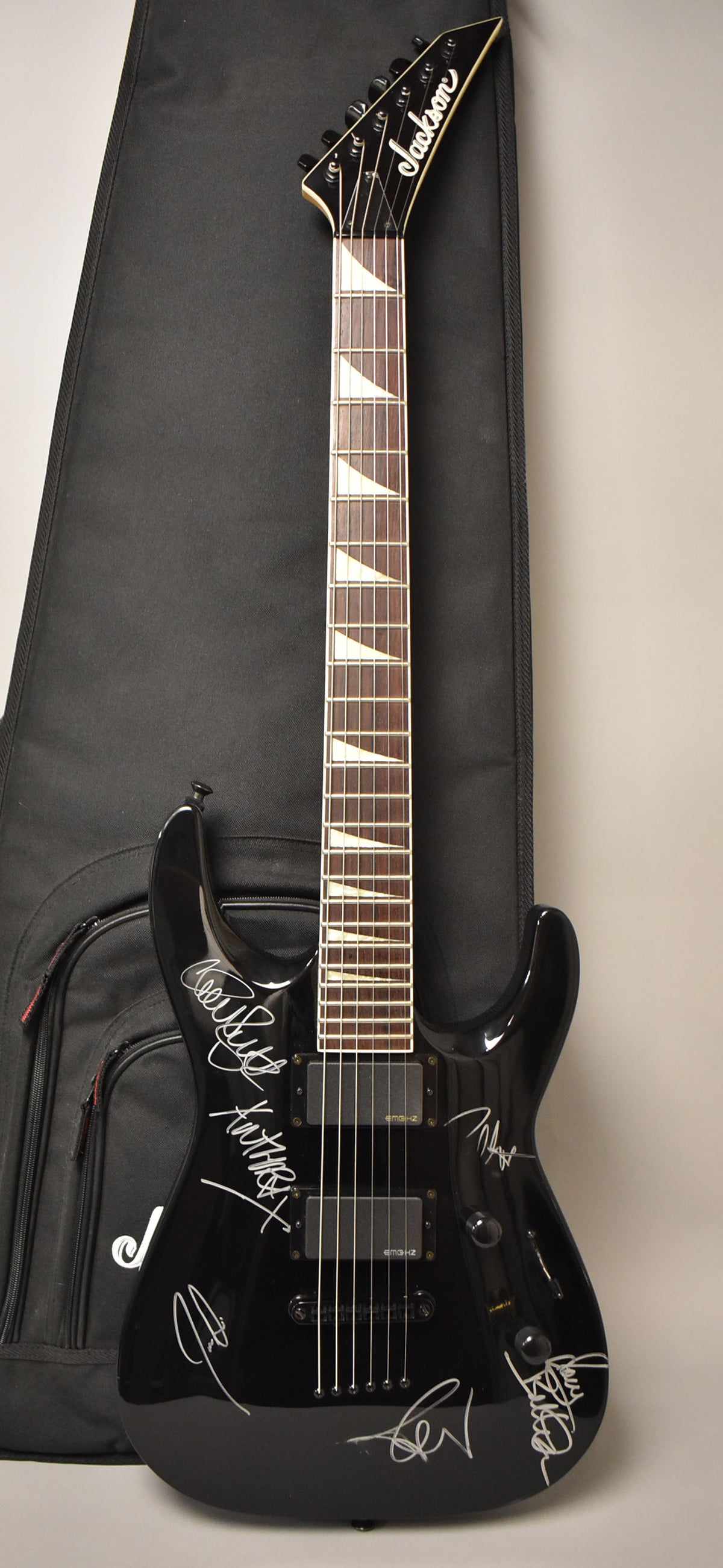 Full-length view of a glossy black electric guitar with white signatures, two humbucker pickups, and triangular fretboard inlays.