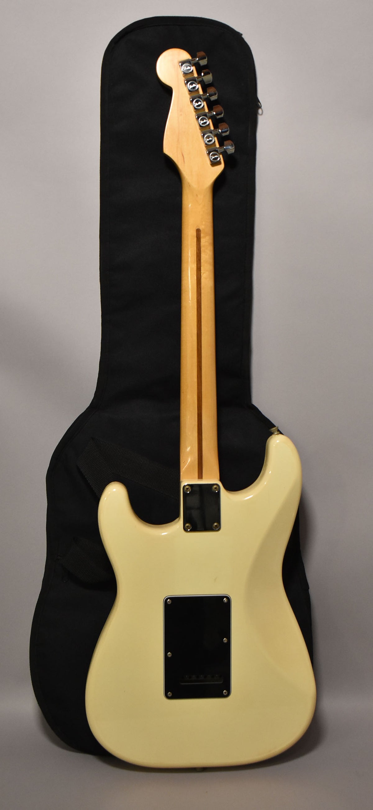 The guitar's back is visible, showing its Arctic White finish, a maple neck with a skunk stripe, and a black tremolo cover.