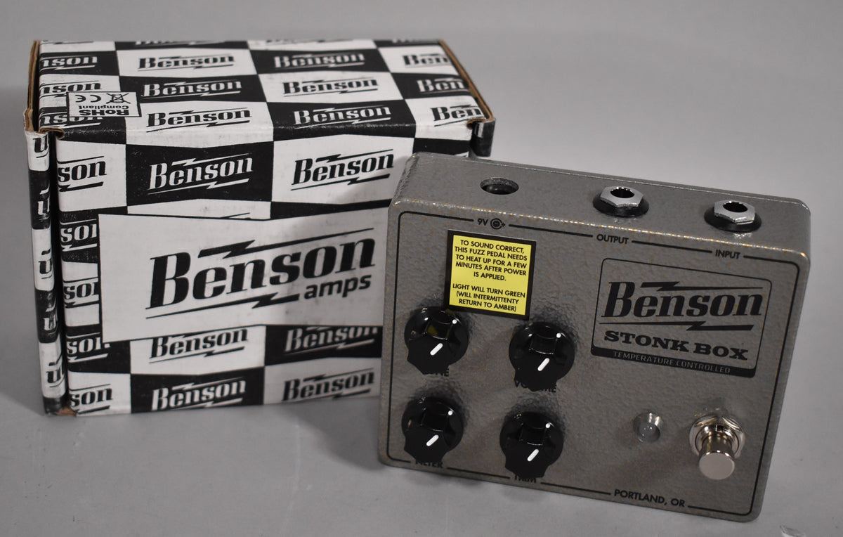 A gray fuzz pedal with four black knobs and a silver footswitch sits next to its black and white checkered box.