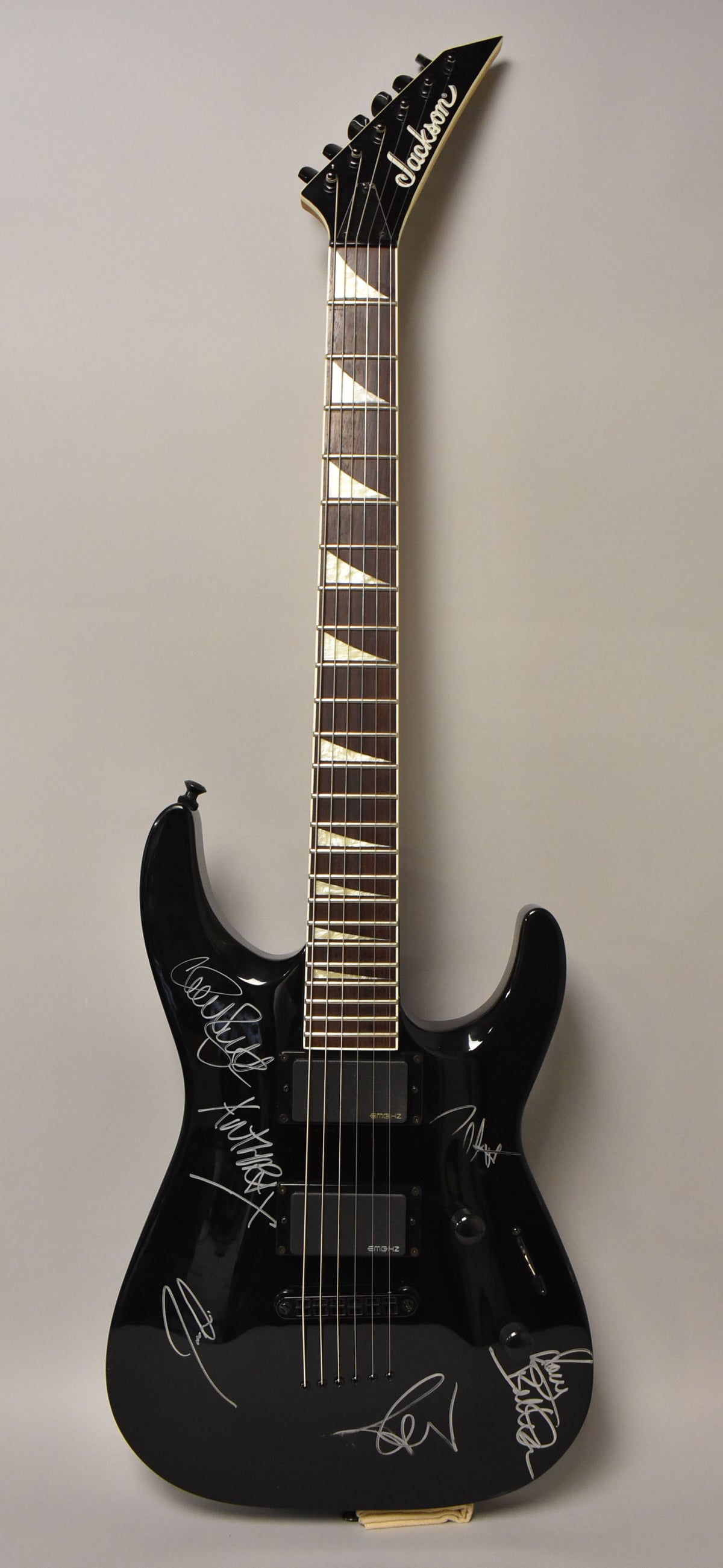 Full-length view of a glossy black electric guitar with white sharkfin inlays and multiple white signatures on the body.