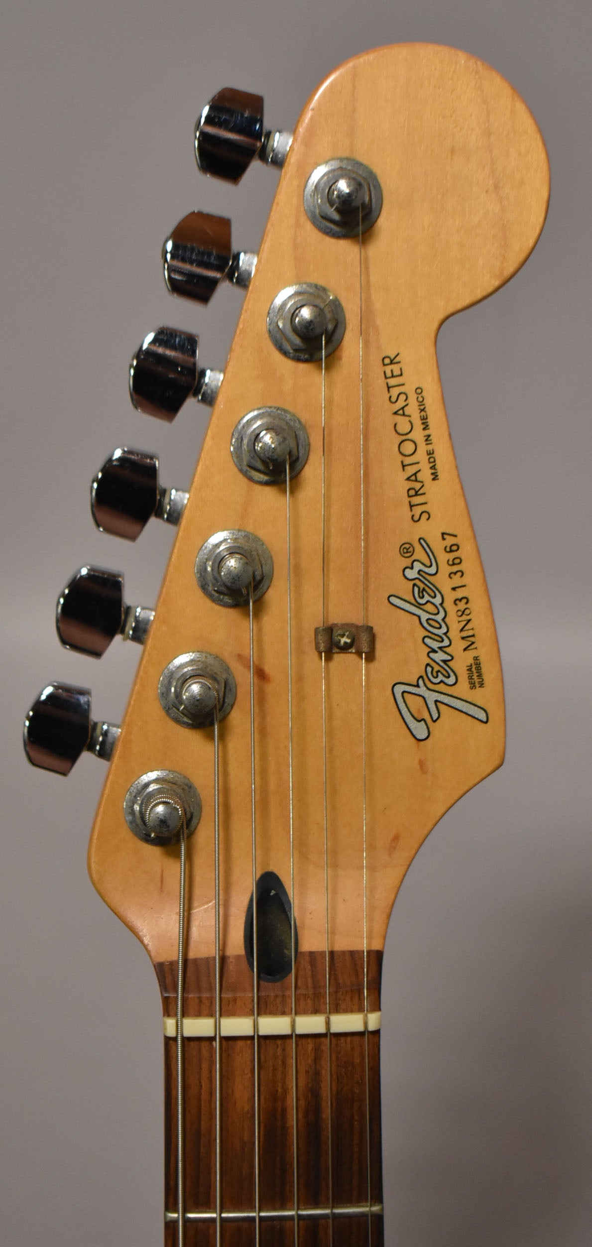 Close-up of the guitar's headstock, showing six chrome tuners, a string tree, and a dark rosewood fretboard with a white nut.