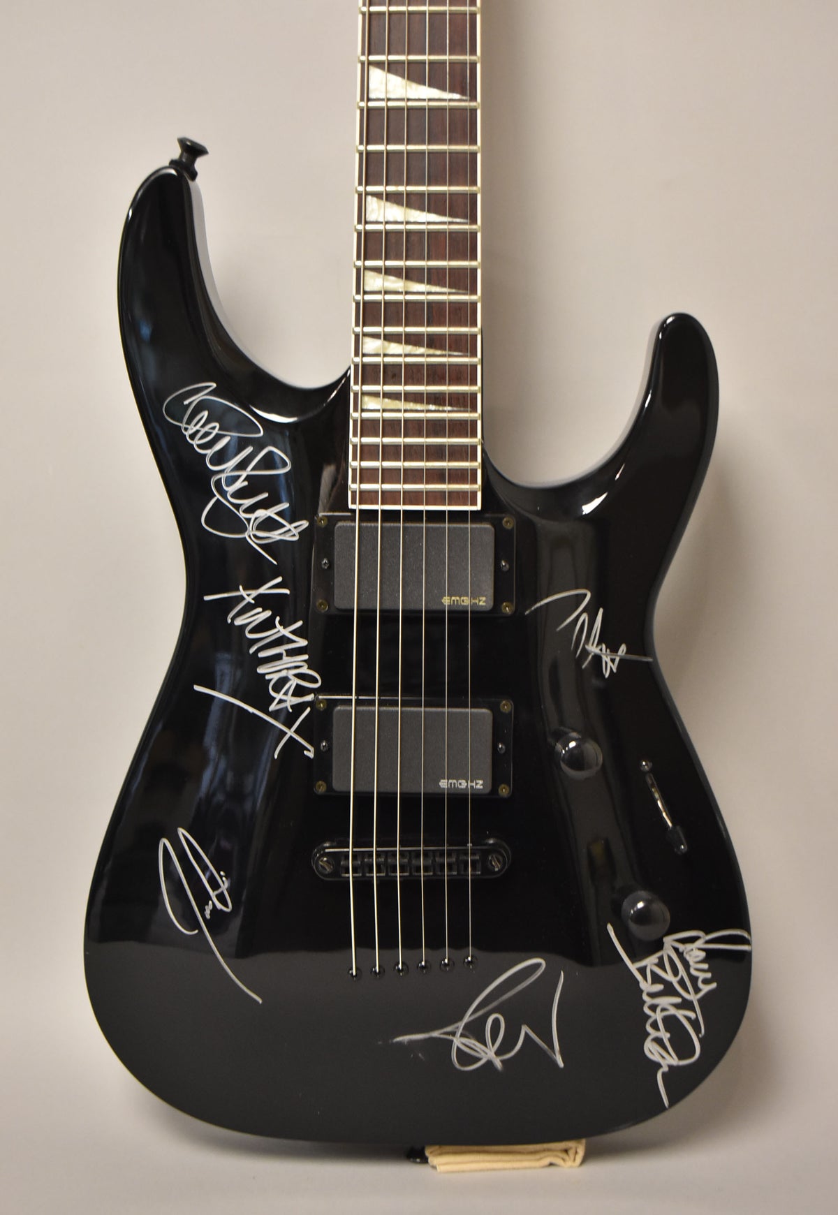 Full front view of a glossy black electric guitar with white signatures, two black humbuckers, and sharkfin fretboard inlays.