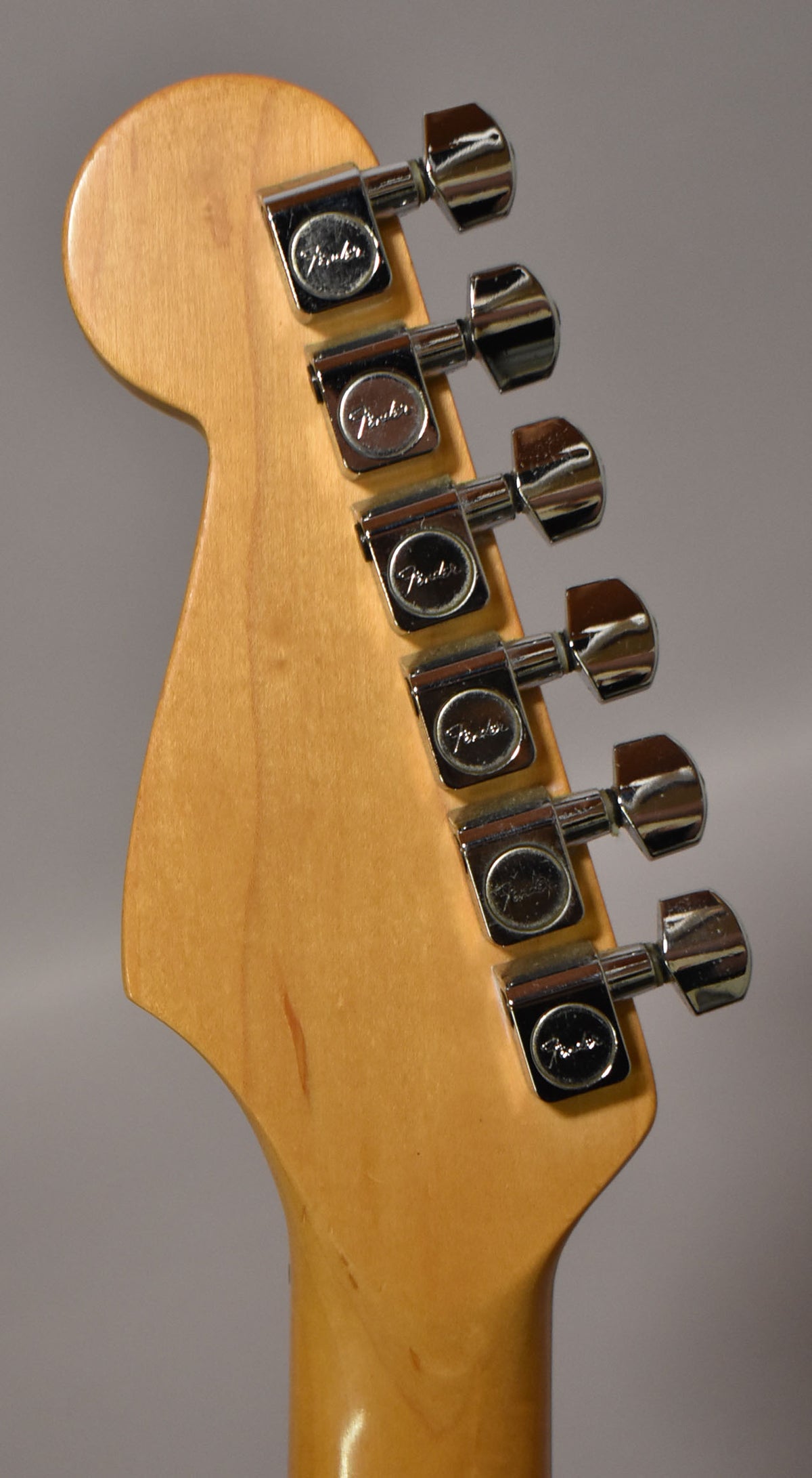 The guitar's light wood headstock is angled left, showing six chrome tuners with light wear and a few small marks on the wood.